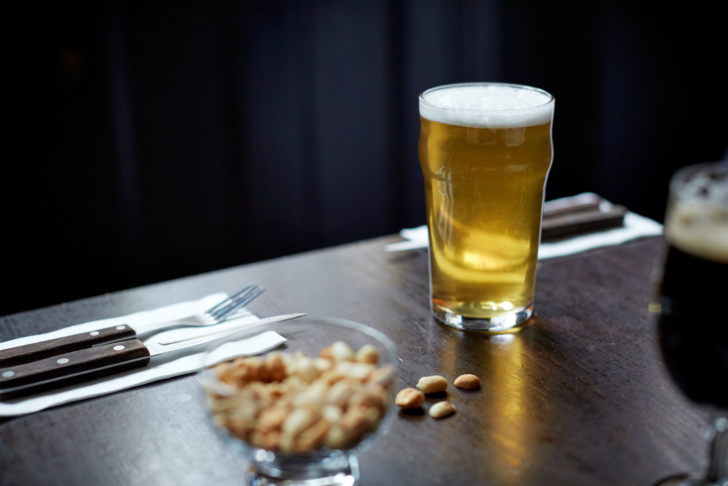 A pint of golden ale on a dark wooden table